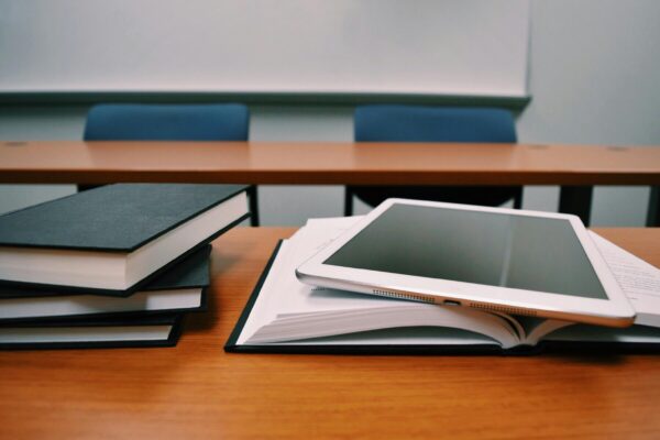 pexels-photo-289737-289737 Books and a tablet on a desk in a classroom, depicting modern education.