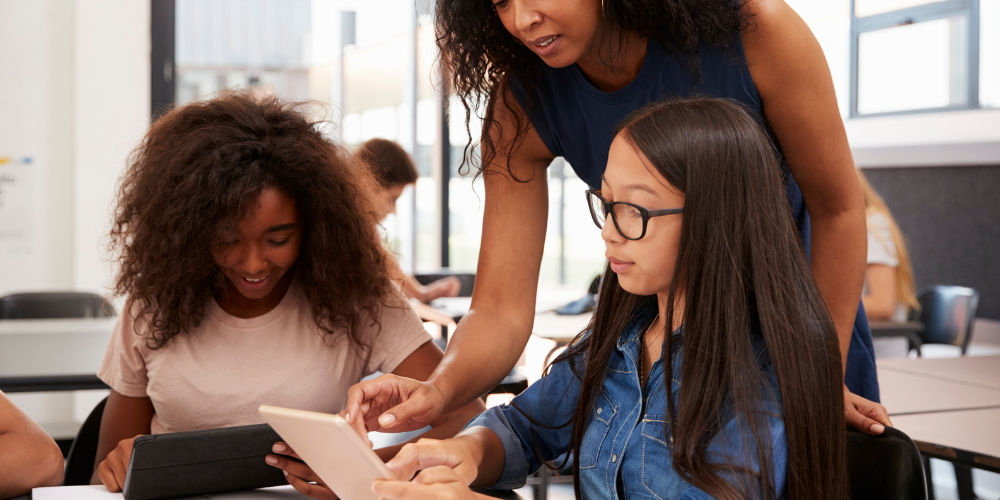 teacher supporting students in learning and using technology in classroom